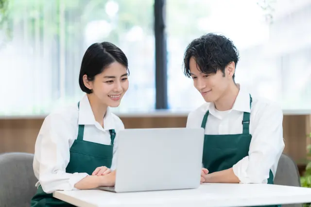 ノートパソコンを見ながら笑顔で話す、カフェの店員2人
